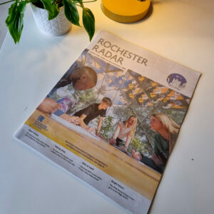 An image showing the Rochester Radar magazine on a table beside a plant and a lamp